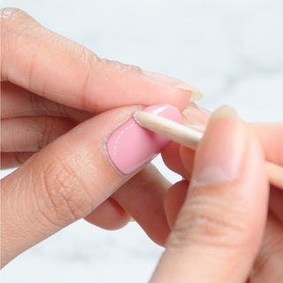 Pressing EyeCandys Gel Nail Sticker with a wooden stick for a smooth, seamless application, ensuring long-lasting, professional-quality nails