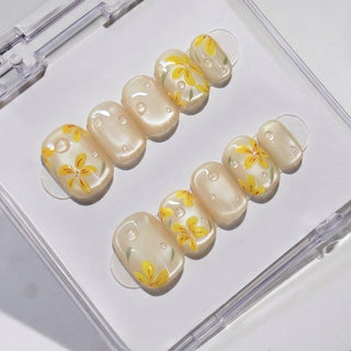 EyeCandys After Rain Press-On Nails feature a pearly base with yellow flower designs and white dots, presented in a clear case—ideal for achieving a salon-quality gel manicure at home with reusable nails.