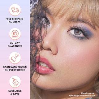 Close-up of a blonde woman in bold makeup, partly veiled by black lace. She wears EyeCandys Bunnie Milky Ash Grey color contact lenses with a glowy design. Perks listed: free shipping, 30-day guarantee, rewards, and subscribe & save.