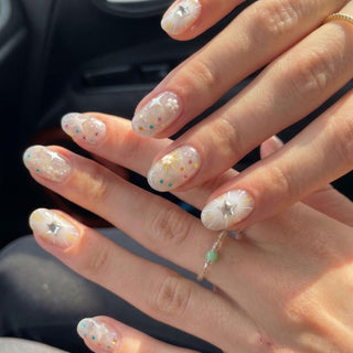 Close-up of hands wearing EyeCandys Constellation Prize Press-On Nails featuring translucent Y2K-inspired designs with colorful star confetti, silver accents, and white and yellow details—an ideal look for instant gel nail style.