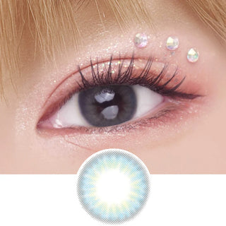 A close-up of an eye wearing EyeCandys Pink Label Mallorca Blue contact lens, glittery pink eyeshadow, long lashes, and three iridescent gems above the lid. A circular image displays the natural-looking lens design below.