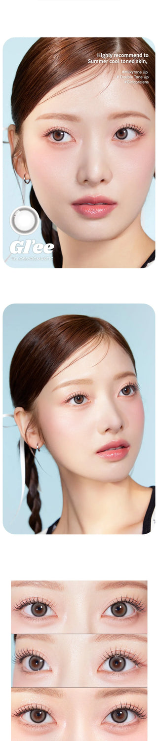 A fair-skinned woman with straight brown hair in a braid wears natural makeup and showcases Olola Glee Grey contact lenses by Olola, which highlight her eyes and dewy complexion against a light blue background.
