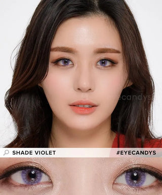 A fair-skinned woman with long dark hair wears EyeCandys Shade Violet Purple contacts. The close-up shows colored contacts for dark eyes. Text reads “SHADE VIOLET” and “#EYECANDYS.”.