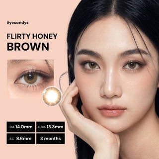 A woman with smooth skin and brown contact lenses poses with her hand on her face. Text reads "EyeCandys Pink Label Flirty Honey Brown"—natural-looking two-tone lenses. DIA 14.0mm, G.DIA 13.3mm, B.C 8.6mm, 3 months.