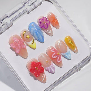 The EyeCandys Flora Bora Press-On Nails set includes ten handmade gel nails with colorful 3D floral designs—pink, purple, blue, and yellow—plus gold accents, stars, and marbled patterns. Comes in a clear plastic case for a salon-quality look at home.