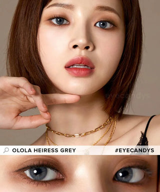 A woman with short brown hair and gold necklaces models Olola Heiress Grey color contacts by Olola for dark eyes. The close-up highlights the colored lenses, with text: "OLOLA HEIRESS GREY" and "#EYECANDYS".