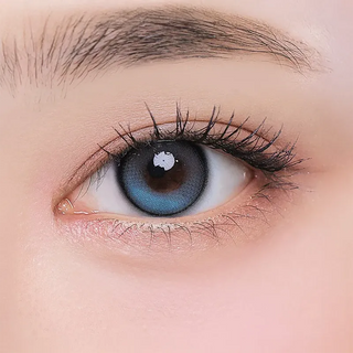A close-up of a human eye with long lashes wearing i-Girl One Pick Balance Forest Tea Blue contact lenses by i-Girl, framed by natural skin and a neat eyebrow, showcasing the fresh Douyin girl style.