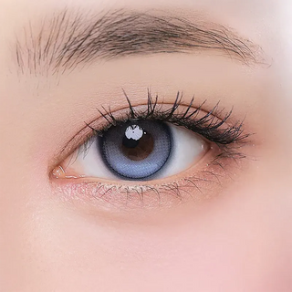 A close-up of a brown eye wearing i-Girl One Pick Balance Summer Song Blue lenses, with long eyelashes and a neatly groomed eyebrow visible at the top.