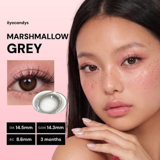 Close-up of a model wearing EyeCandys Pink Label Marshmallow Grey contacts with natural makeup. The image spotlights her eyes, features an inset lens photo, product specs, and "MARSHMALLOW GREY" on a pink background.