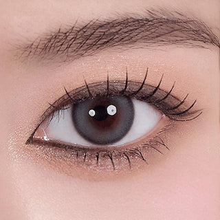 Asian eye wearing Melinoe 1-Day Beige Blue coloured contact lens on top of a dark iris, with natural glitter eyeshadow and long eyelashes.