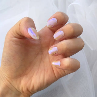 A hand with short, oval nails wears EyeCandys Melon Magic Gel Nail Sticker Set in a shiny pastel chrome finish, reflecting pink, purple, and white hues. The background is soft sheer white fabric.