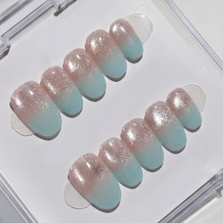 Mist n Fade Press-On Nails by EyeCandys feature a handmade pink-to-blue ombre with a shimmery glitter finish, arranged in two rows inside a clear plastic case.