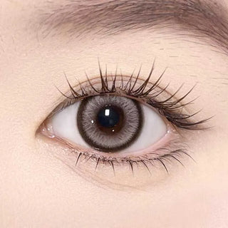 A close-up of a human eye wearing Olola Meow Vivid Aby Brown myopia prescription colored contact lenses by Olola, showcasing long eyelashes, a vivid iris design, and smooth skin around the eye.