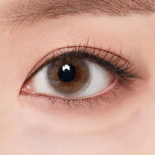 A close-up of a person’s brown eye with long lashes and natural makeup, wearing Olola Able Grey color contact lenses by Olola for myopia, highlighting the detailed skin texture around the eye.