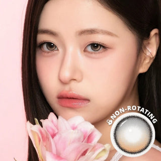 A young woman with long dark hair holds a pink lily near her face, showcasing smooth skin, soft makeup, and i-Sha One Pick Only One Cherry Choco 3-tone gradient lenses for natural eye enlargement. A “Non-Rotating” graphic appears below.