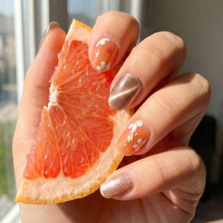 Hand wearing reusable Peachy Keen press on nails featuring daisy floral design, jelly base, gold foil flakes, and warm summer tones.