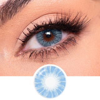 A close-up of a blue eye with bold red and gold eyeshadow, long lashes, and light pink hair partly over the brow. Below is EyeCandys Shade Blue by EyeCandys, a high-coverage blue contact lens perfect for dark eyes.