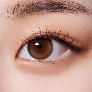 A close-up of a brown eye with long lashes and natural makeup, enhanced by Olola Purity Shine 1-Day Hazel Brown (10pk) color contact lenses for myopia.