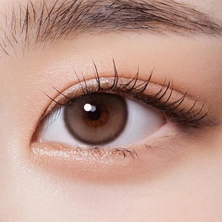 A close-up of an eye with natural makeup, long lashes, and Olola Purity Shine 1-Day Taupe Brown contact lens by Olola. This daily disposable lens offers a smooth finish and is suitable for myopia prescription users.