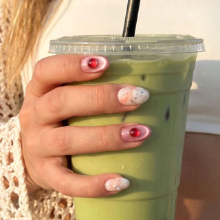 Hand wearing EyeCandys Raspberry Ripple press on nails featuring peach cream marble swirl, rose cat eye nails, and raspberry glitter dome bead accents.