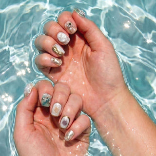 Hand wearing EyeCandys Shell We press on nails featuring pearl textured nails, shell design, and gold and silver accents.