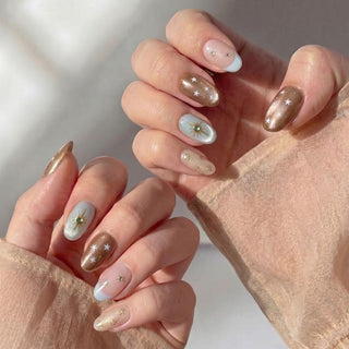 A pair of hands wears EyeCandys Space Bar Press-On Nails in pastel blue and nude with gold and white star accents plus gems, creating a flawless mani. The person is dressed in a sheer beige long-sleeve top.