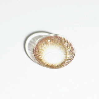 The EyeCandys Pink Label Vintage Brown contact lens, featuring a brown and yellow pattern, stands upright on a white surface with a soft shadow—ideal for achieving a subtle dolly look.