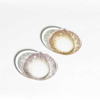 Two Pink Label Vintage Brown contact lenses by EyeCandys, featuring a light brown and yellow gradient design, rest on a white surface and cast soft shadows beside them.