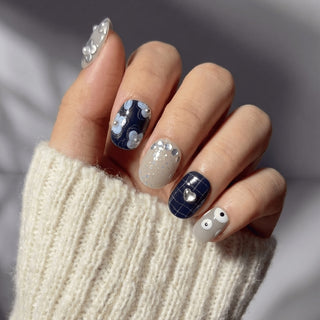 Stylish hand wearing EyeCandys All Tied Up press on nails with greige base, marble heart nail, ribbon bows, and illustrated eye detail.