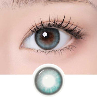 A close-up of an eye with long lashes wearing i-Girl One Pick Becca Matcha Blue contacts in a blue-gray shade. An enlarged image of the i-Girl lens is shown below the eye for detail.