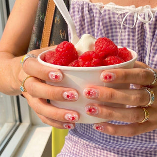 Close up hand showcasing EyeCandys Catching Feelings press on nails with peach jelly base, red hearts, and pink glitter wash.