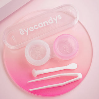 The EyeCandys Contact Lens Case Applicator Kit features a pink and white contact lens case, along with branded lens tweezers, an applicator wand, and a clear plastic storage box—all stylishly arranged on a pink gradient surface.