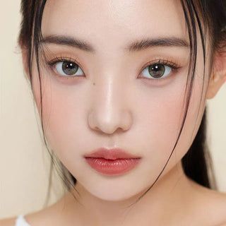 A young woman with fair skin, straight black hair, and soft pink lips wears Gemhour Demeter 1-Day 13.5 Olive Green contacts (10pk), looking directly at the camera against a neutral background.