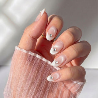 Hand wearing Eyecandys Front Row press-on nails with a sheer nude base, shimmering white cat-eye French tips, crystal accents, and a salon-quality short oval shape.