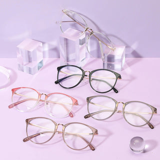Five pairs of EyeCandys Infinity Oversized Oval eyeglasses, featuring vintage-inspired thin metal frames in various colors, are displayed on a purple surface with clear acrylic blocks and a glass sphere for a modern, stylish look.