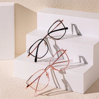 Two pairs of EyeCandys Kaylee Cat Eye glasses, one in black and one in rose gold, are shown on white geometric steps against a textured beige background, with soft shadows highlighting these fashionable eyeglasses.
