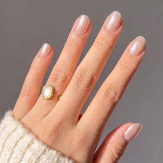 Hand wearing Eyecandys Silk Slip press-on nails with a luminous champagne pink chrome finish, glazed effect, and salon-quality short oval shape.