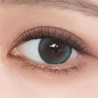 A close-up of a human eye with natural makeup and long lashes wearing Gemhour Demeter 1-Day 13.0 Ocean Blue (10pk) contacts, which have a dark outer rim and grayish center for an enlarged, defined iris effect.