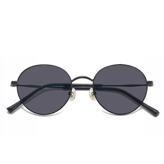 The EyeCandys Luna Round features round black sunglasses with dark lenses, a thin metal frame inspired by classic eyeglasses, and adjustable nose pads, displayed facing forward on a plain white background.