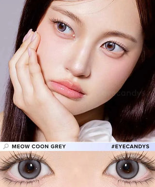 A woman with fair skin and straight dark hair rests her face on her hand, wearing Olola Meow Natural Coon Grey contacts by Olola. A close-up showcases the natural cat-eye look. Text reads "MEOW NATURAL COON GREY #EYECANDYS".