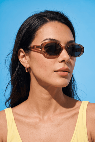 Model wearing EyeCandys Jellicle Oval coffee full-frame sunglasses. Lightweight TR oval frames with a minimalist 90s-inspired unisex design, ideal for diamond and heart face shapes.