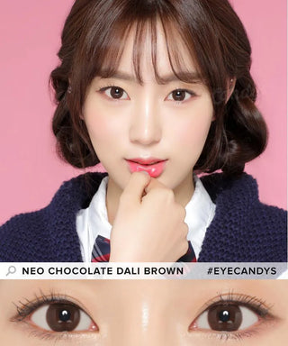 A young woman with fair skin and brown hair poses before a pink background, highlighting her brown eyes enhanced by NEO Vision Dali Chocolate Brown lenses—a must-have from NEO Vision for lovers of Korean makeup.