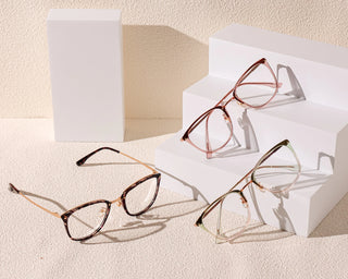Three pairs of EyeCandys Posh Square full-frame glasses in various colors are displayed on white geometric blocks and a textured beige surface under soft lighting.