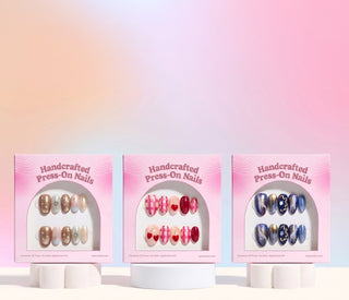 EyeCandys press on nails assortment on pink backdrop showcasing trending reusable nail sets with floral, chrome, marble, and glitter nail designs.