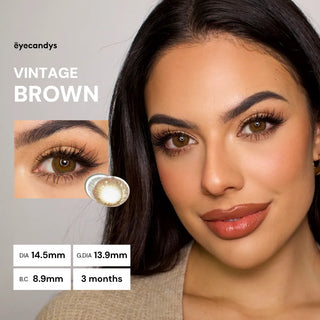 A woman with long dark hair and flawless makeup wears EyeCandys Pink Label Vintage Brown color contacts. These lenses give a soft, dolly look with a 14.5mm diameter, 13.9mm graphic diameter, 8.9mm base curve, and last for 3 months.