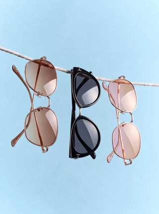Three pairs of oval eyeglasses in different colors—black, tortoiseshell, and translucent gray—are floating against a neutral background with soft shadows.