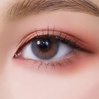 A close-up of a human eye wearing Olola Able Blue contact lenses by Olola, featuring light brown and blue tones, subtle peach eye makeup, long lashes, and a well-groomed brow—perfect for those seeking lenses for dark eyes.