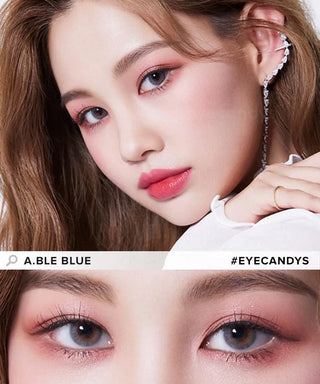 A woman with long brown hair wears Olola Able Blue color contact lenses and pink makeup. The top half shows her face and ear cuff, while the bottom half is a close-up of her blue eyes. Text: “Olola Able Blue #EYECANDYS.”.
