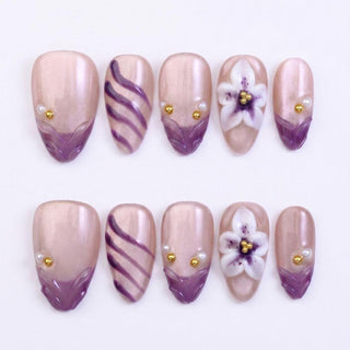 The EyeCandys Aloha Darling Press-On Nails set includes 10 handmade nails with a shimmery nude base and purple tips, wavy purple lines, pearl and gold beads, plus 3D white and purple floral accents for a salon gel look. White background.