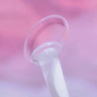 The EyeCandys Limited Edition Amelie Sakura Jelly Pink (1 PAIR) contact lens is displayed on a white applicator against a softly blurred pink and purple background.